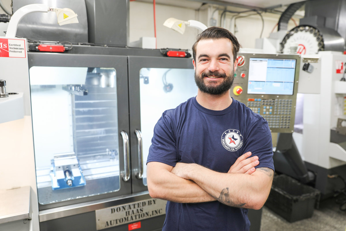 Army veteran Isaiah standing in front of Haas CNC machine at Workshops for Warriors