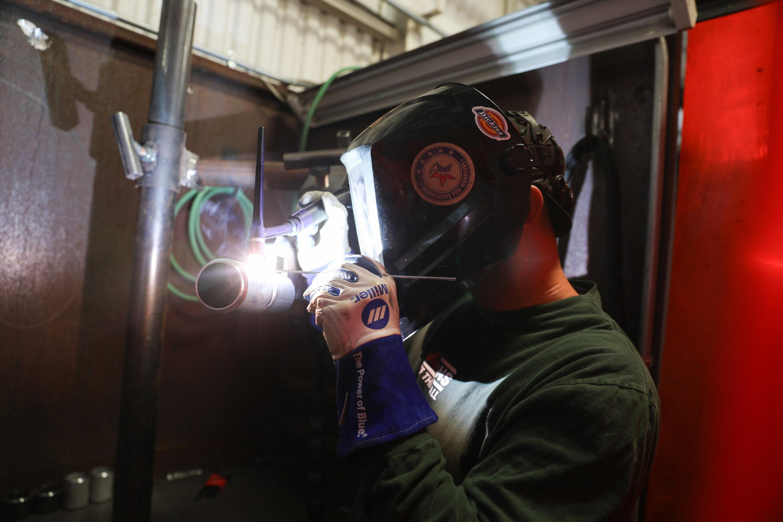 Veteran and welder Kenneth wearing helmet and welding in booth at Workshops for Warriors